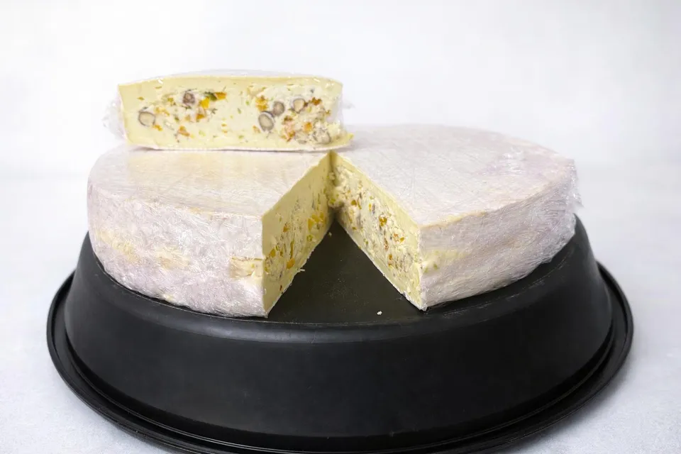 Meule de fromage à pâte crémeuse entamée, fourrée de fruits secs et de noix, présentée sur un plateau noir