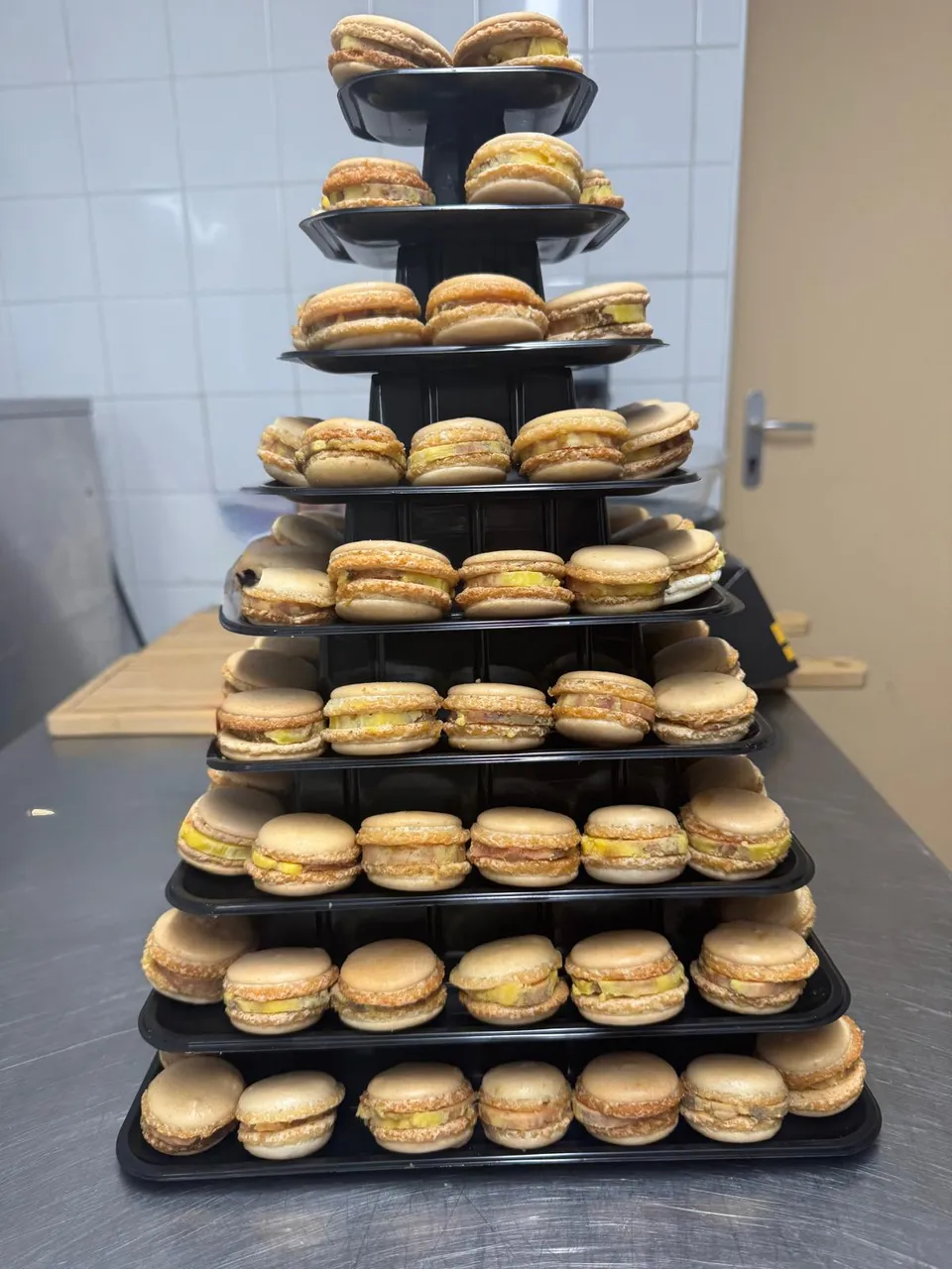 Pyramide de macarons garnis dressée sur un présentoir noir à étages, en cuisine avant le service