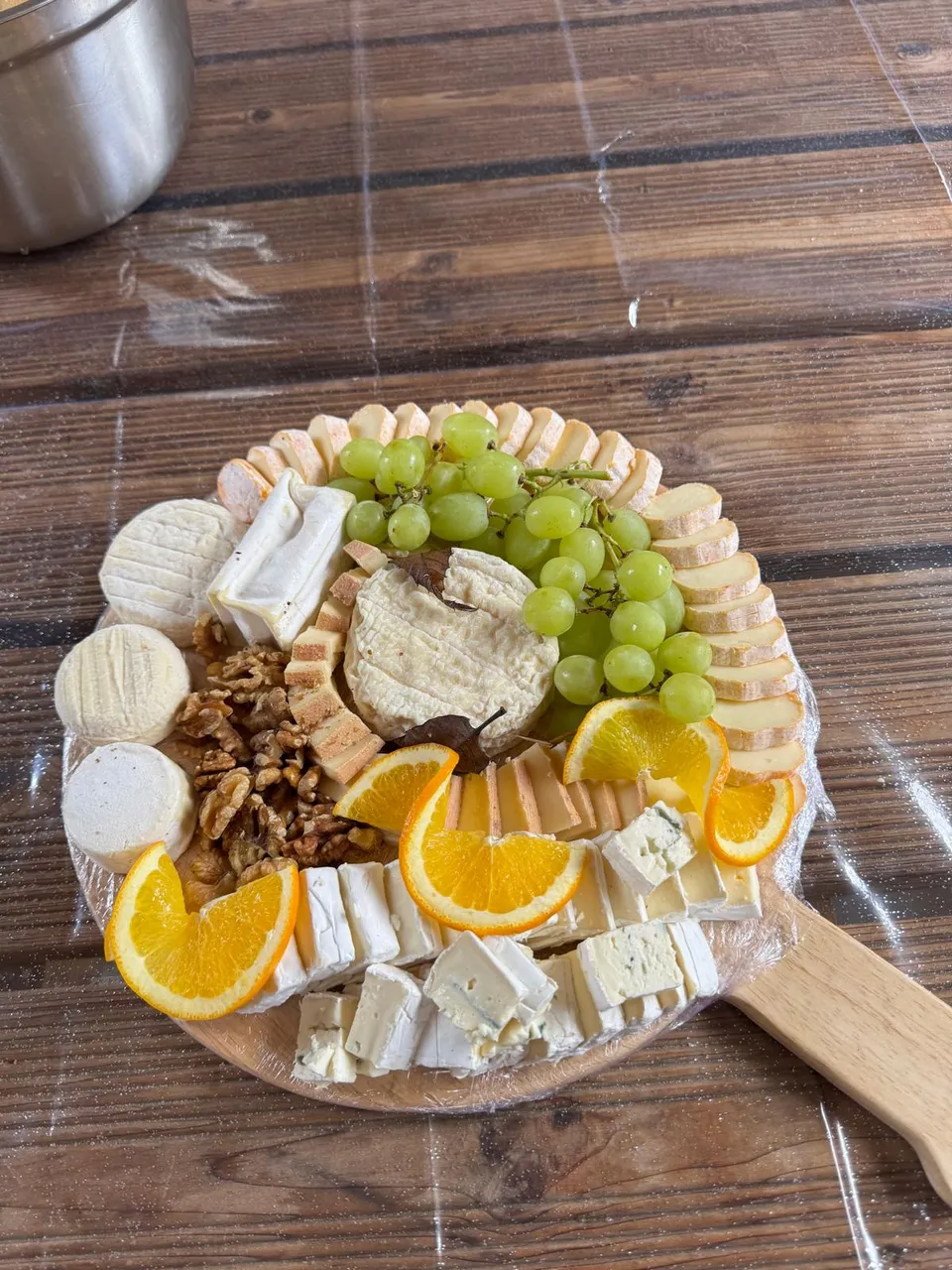 Petit plateau de fromages sur planche en bois : pâtes molles, cerneaux de noix, raisin blanc et tranches d’orange