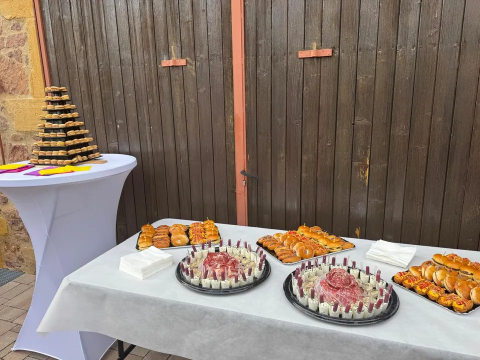 Table de buffet en extérieur : plateaux de jambon cru entourés de verrines, mini burgers, brioches garnies et pyramide de macarons