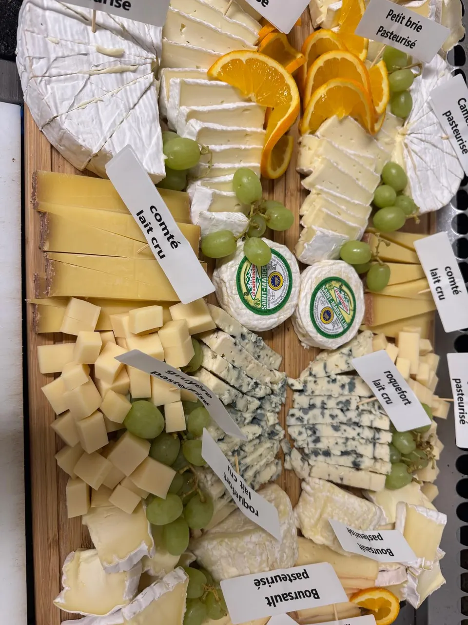 Grand plateau de fromages étiquetés : camembert, petit brie, comté au lait cru, roquefort, Boursault, raisin et oranges