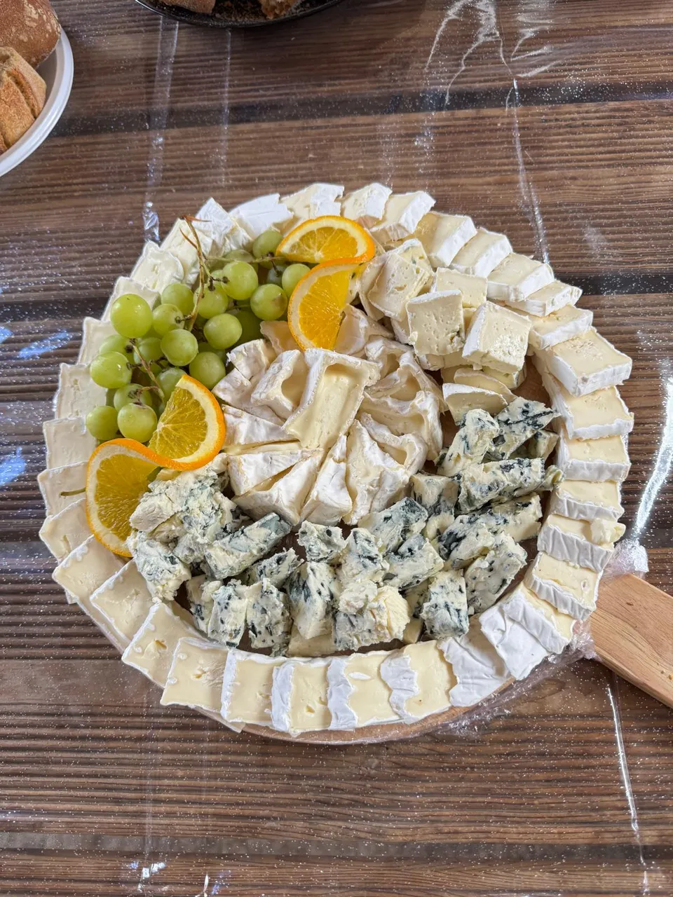 Plateau rond de fromages : bordure de brie, cœur de bleu en morceaux, fromages crémeux, raisin blanc et tranches d’orange