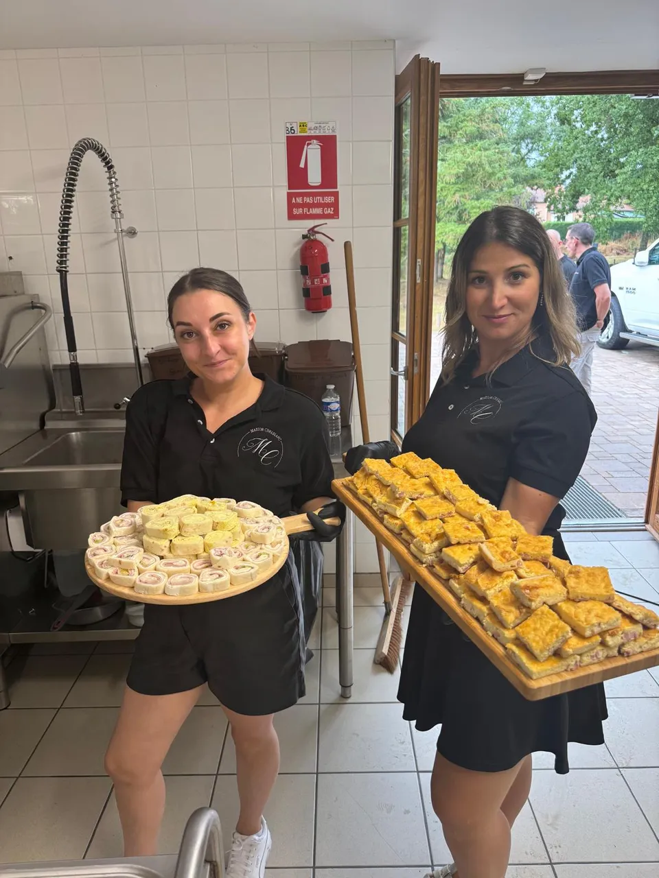 Deux membres de l’équipe Maison Cherblanc présentent des planches de wraps roulés et de carrés salés gratinés en cuisine