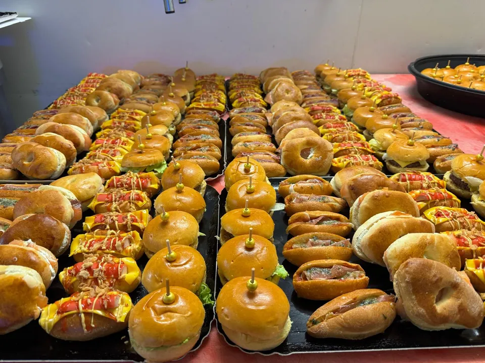 Plaques de mini burgers, mini hot-dogs et bagels garnis alignées sur une table avant le service d’un buffet
