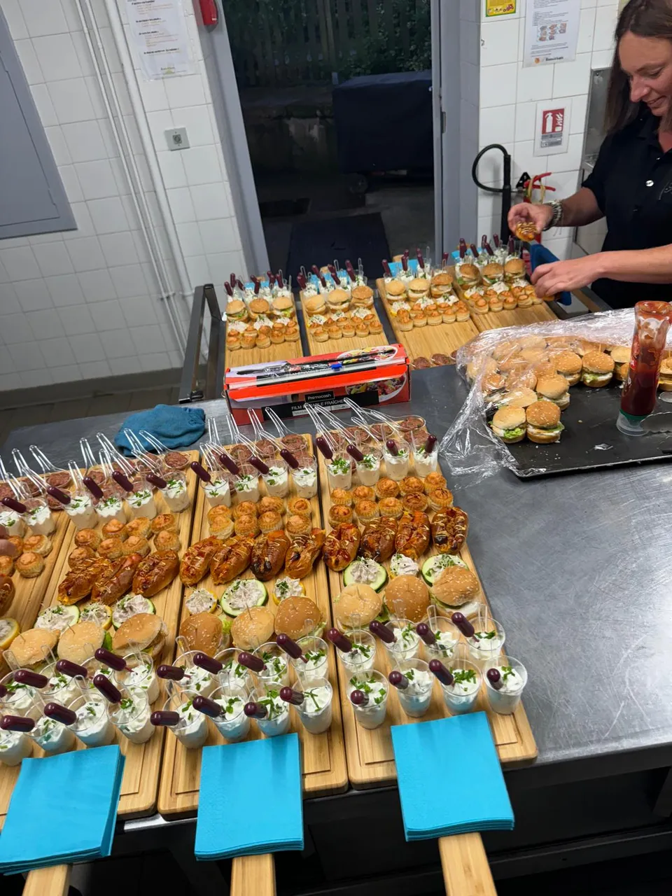 Planches apéritives en cours de dressage en cuisine : verrines, mini burgers, brioches garnies et bouchées salées
