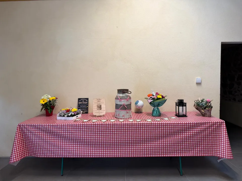 Table d’accueil décorée : nappe vichy rouge, bouquets de fleurs, bidon à lait habillé de ruban, lanterne et ardoise décorative