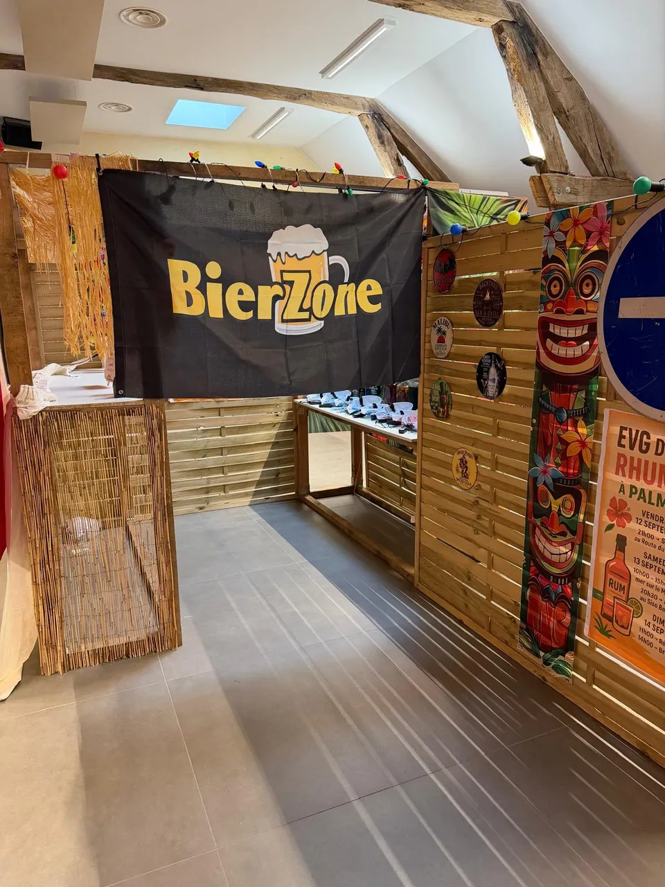 Espace bar à bière décoré pour une soirée : banderole BierZone, comptoir en bois, masques tiki et guirlandes lumineuses